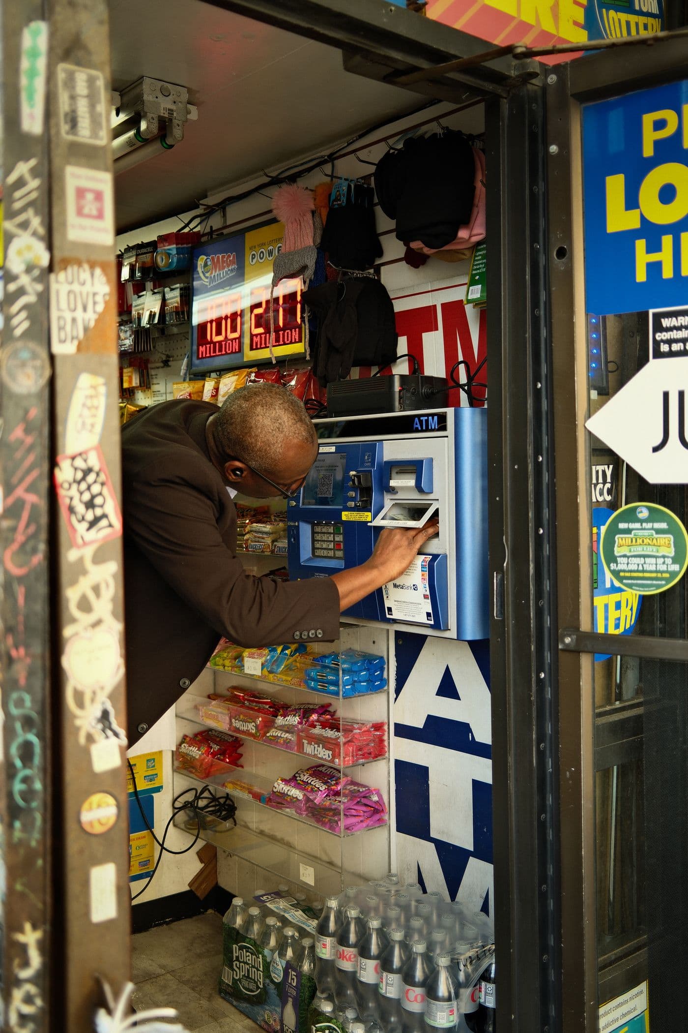 A customer using the in-store ATM with lotto signage and shelves of snacks and water around them